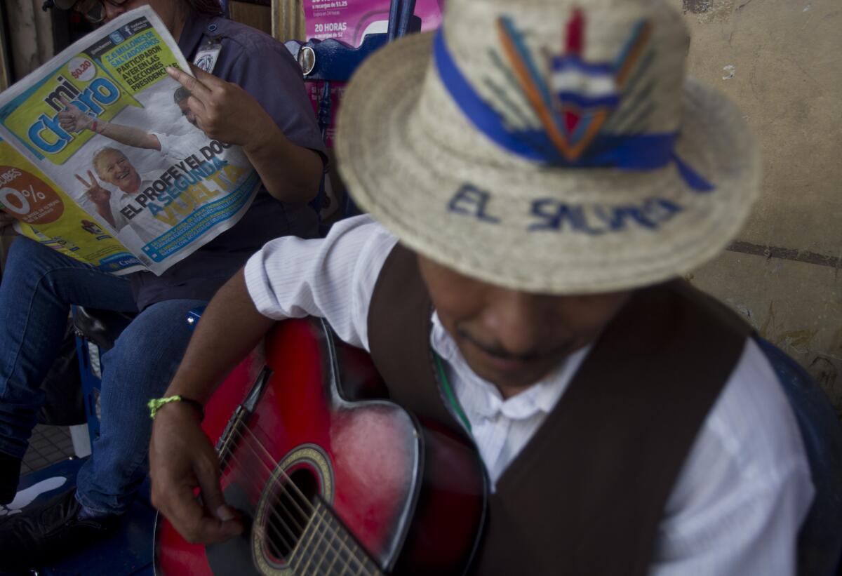 A Salvadoran woman reads a newspaper with election results, while a man plays guitar in San Salvador, El Salvador. The presidential election appears to be headed for a runoff.