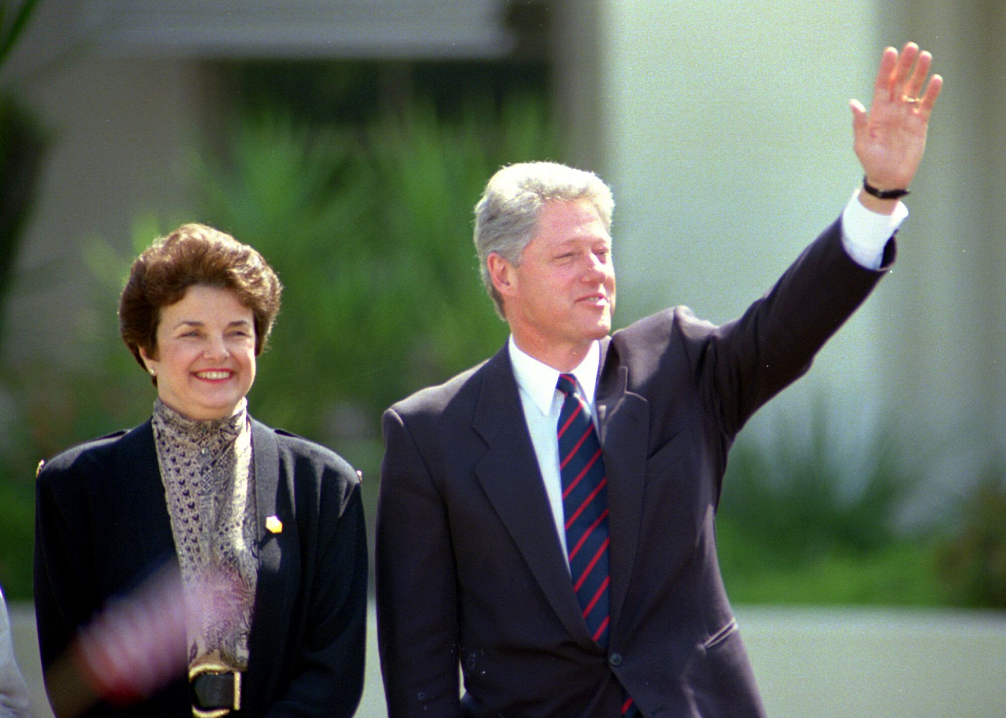 At right, Bill Clinton waves and California Sen. Dianne Feinstein stands at left, both smiling. 