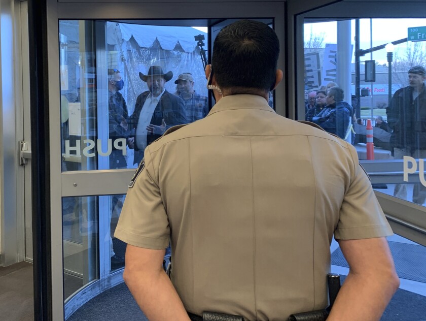 Anti-government activist Ammon Bundy, wearing a cowboy hat, yells through the closed Ada County Courthouse door at law enforcement officers inside Monday, March 15, 2021, in Boise, Idaho. Bundy was scheduled to stand trial Monday on charges that he trespassed and obstructed officers at the Idaho Statehouse during a special legislative session last fall, but Magistrate Judge David Manweiler issued a warrant for Bundy's arrest after Bundy failed to appear in the courtroom. People are required to wear face coverings while at the courthouse because of the coronavirus pandemic, but Bundy and several others were protesting the mask requirement. (AP Photo/Rebecca Boone)