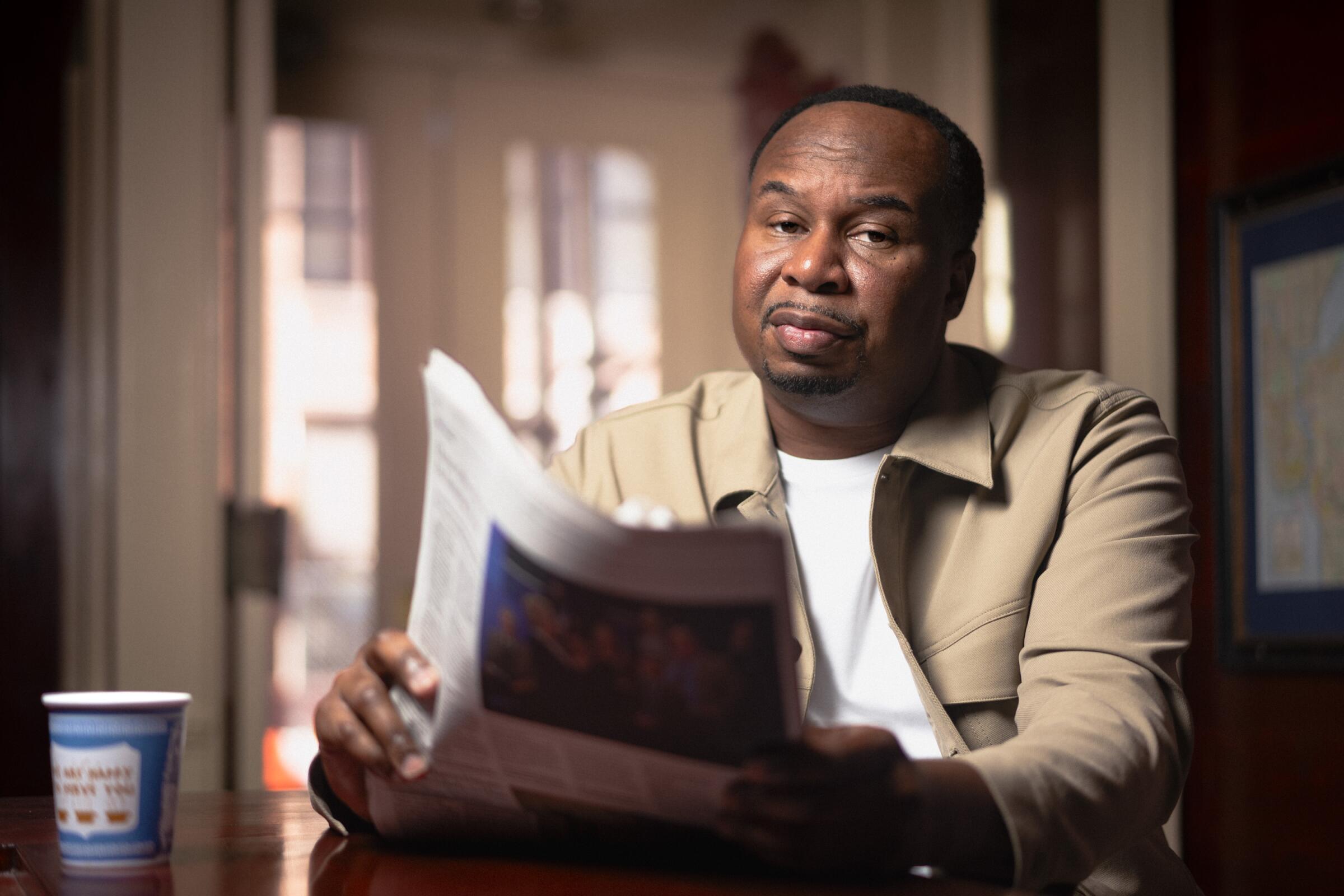 Roy Wood Jr. sits and holds a newspaper.