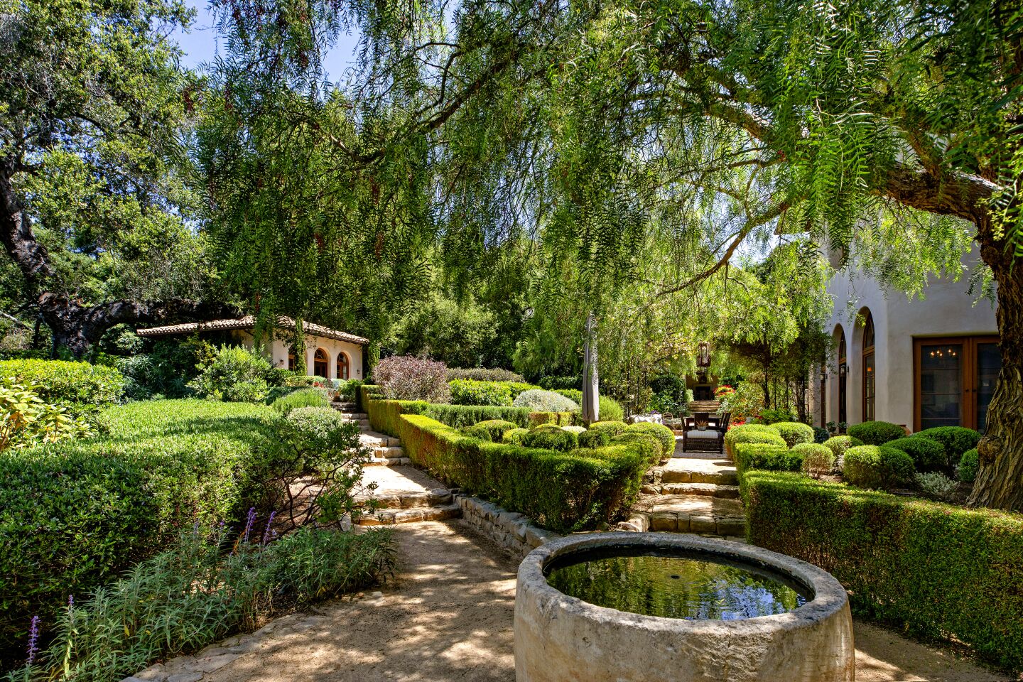 A stone fountain and paths lead through the gardens outside the Mediterranean villa-style home