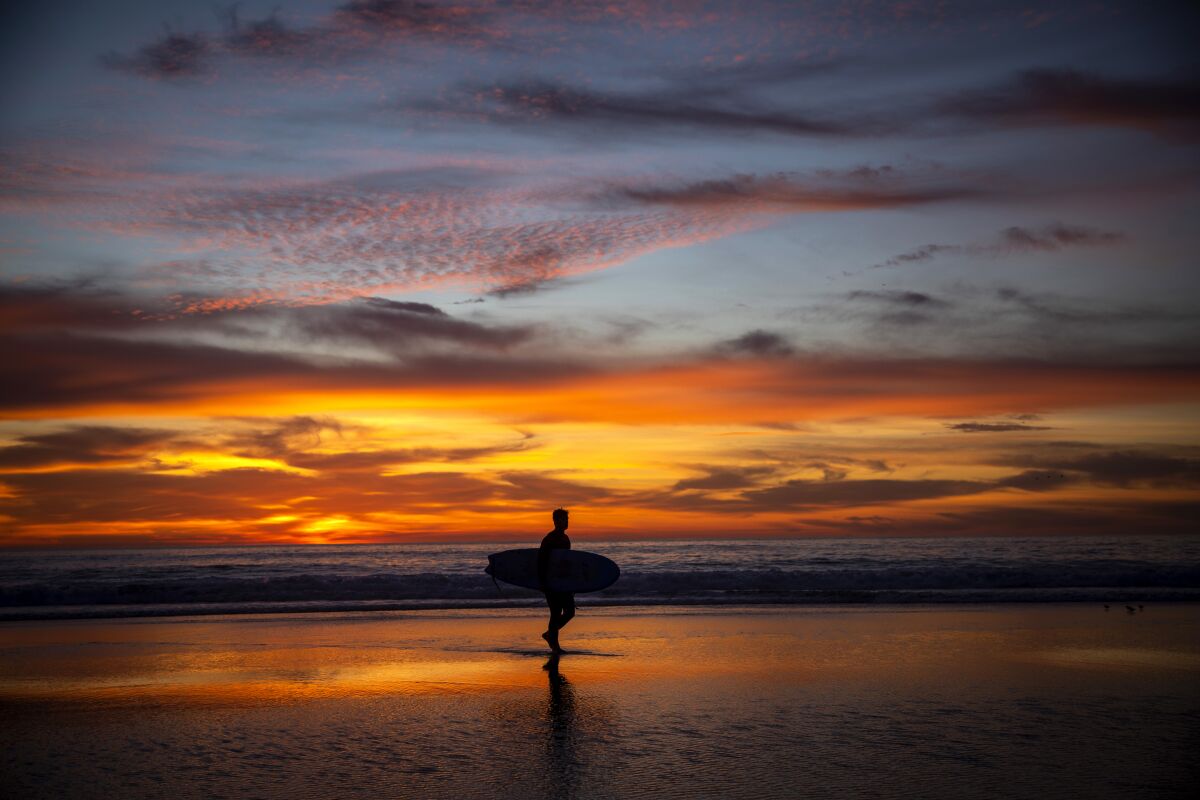 Surfer holding board with sunset in background