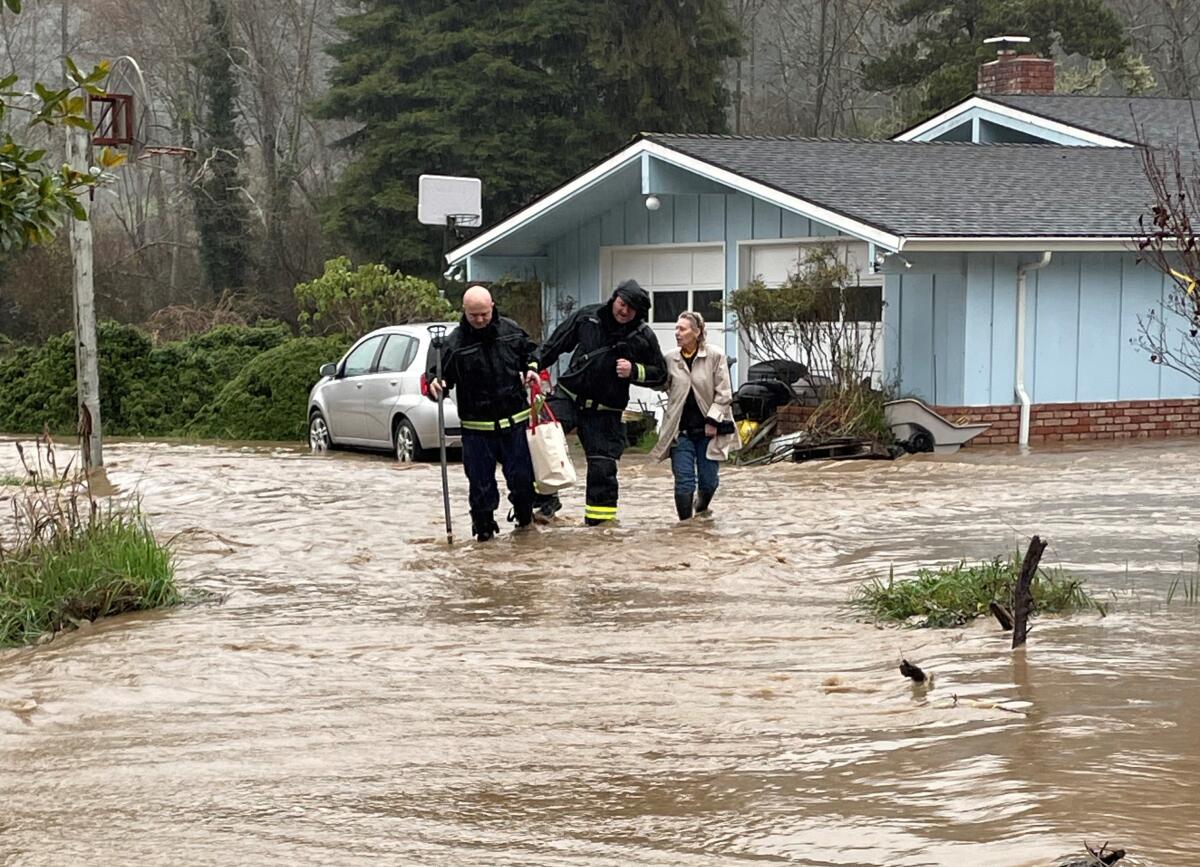 Firefighters assist a resident amid flooding.