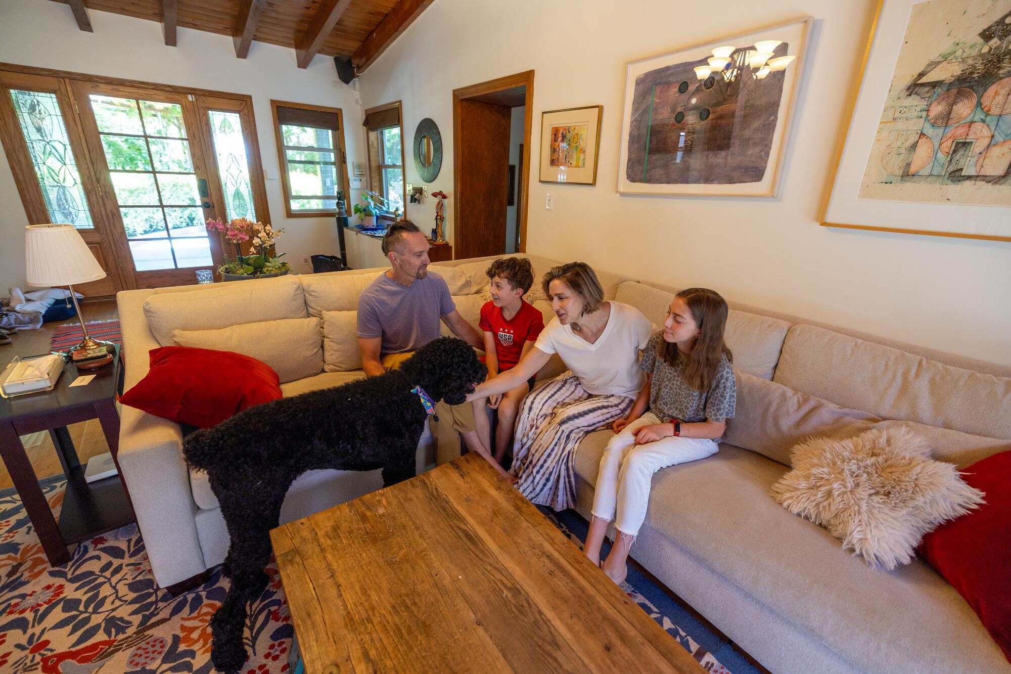 Family members sit on a sectional and pet their dog.