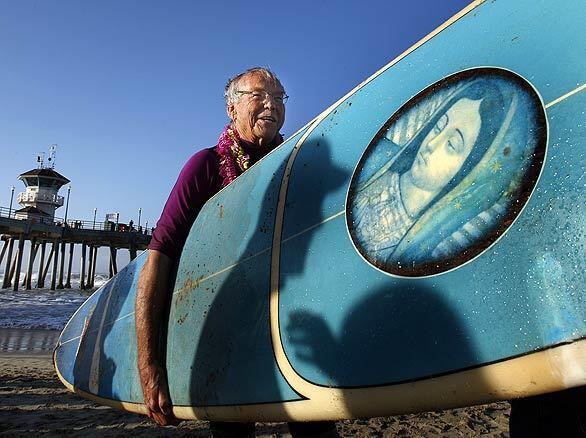 HOPE FLOATS: Father Christian Mondor of Sts. Simon and Jude Catholic Church carries Father Matt Munoz's surfboard, which bears an image of the Virgin Mary, along the beach after the "blessing of the waves" ceremony at the Huntington Beach Pier.