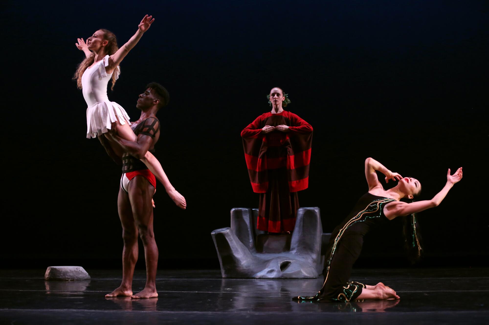 Four dancers are on stage with a dancer being held up to the left. 