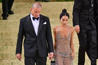 Channing Tatum in a tuxedo walking down golden stairs next to Zoê Kravitz in a sheer net gown. 