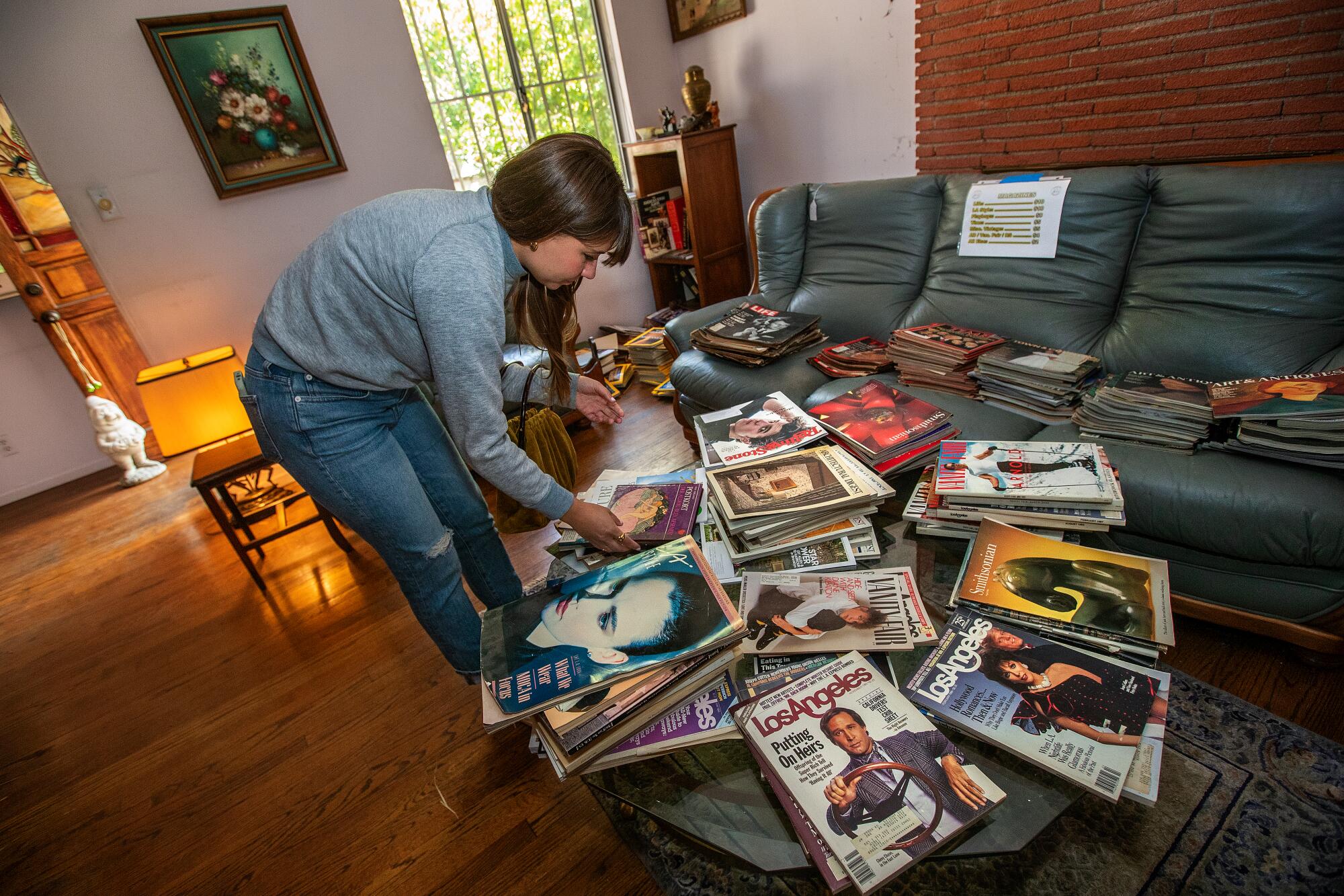 Amy Solomon bending over a coffee table, looking at old magazines in a house.
