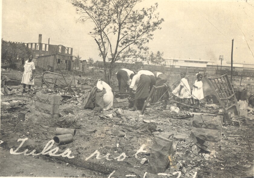 A black-and-white photo from 1921 shows a few people searching through post-riot rubble in Greenwood, Okla.