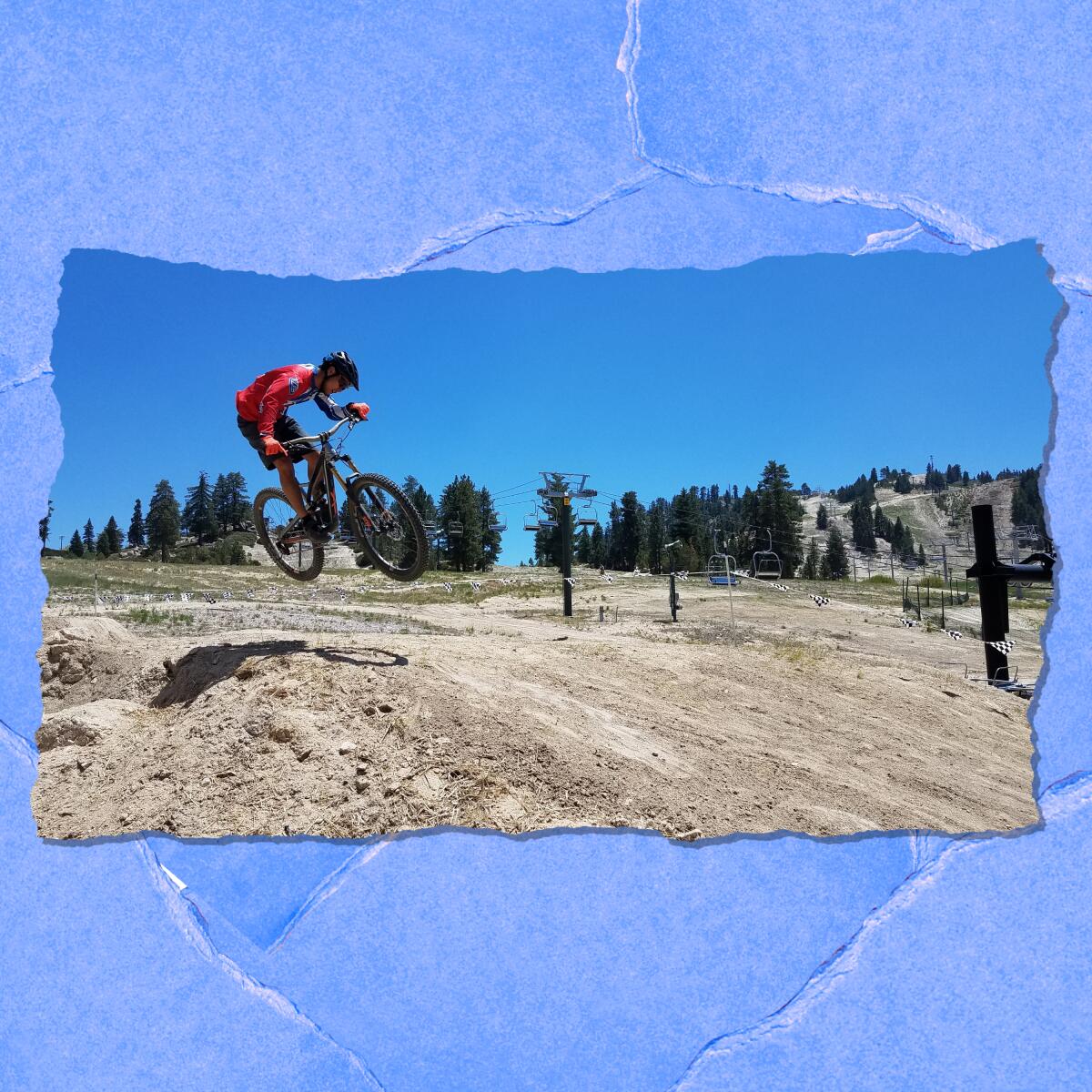 A rider propels a dirt bike over a hill. In the background are evergreen trees and low mountains.