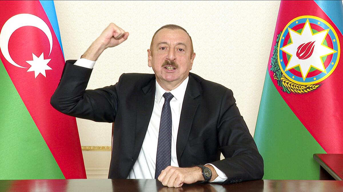Azerbaijani President Ilham Aliyev raises his fist while seated with flags on either side of him.