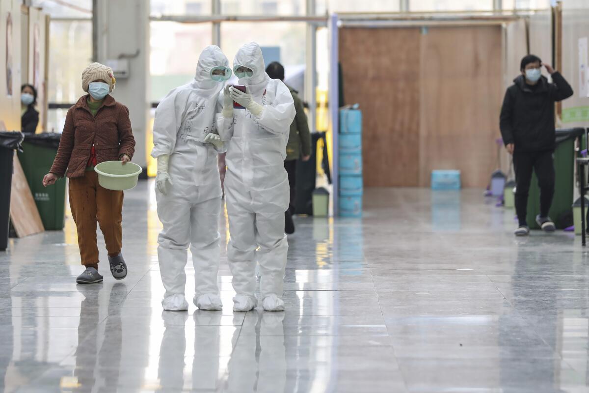 In this Friday, Feb. 21, 2020, photo, nurses in protective suits look at a smartphone at a temporary hospital at Tazihu Gymnasium in Wuhan in central China's Hubei province.