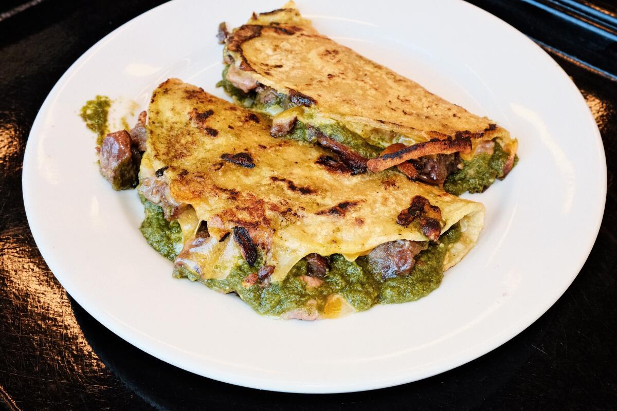 Two taco type "folding" Stuffed beef cheek, cheese and green herb sauce on a black platter at Locol in Watts