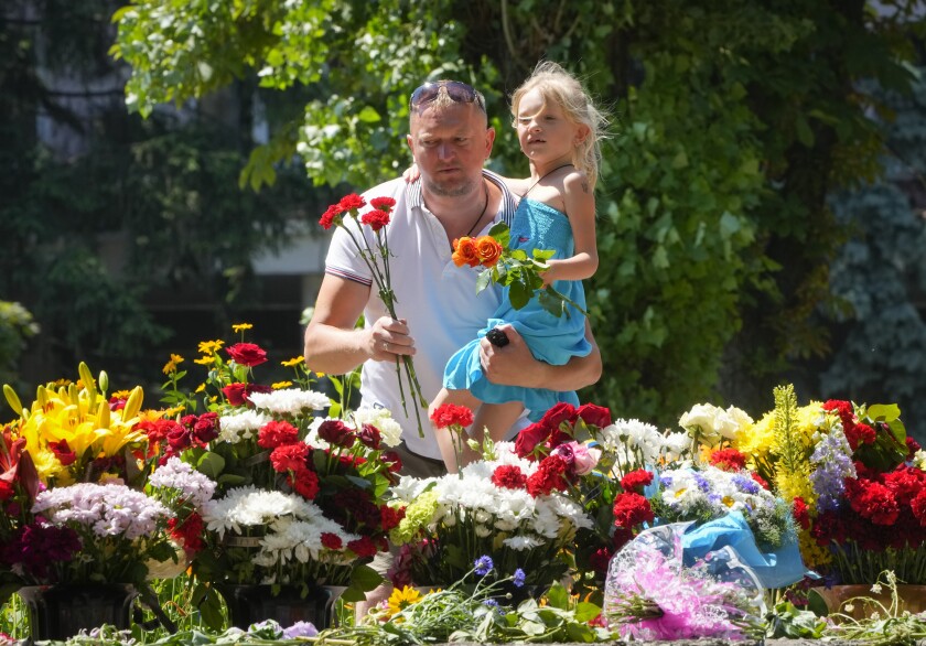 A man holding a little girl, both are adding flowers to a memorial.