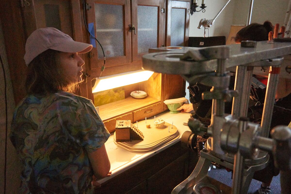 A woman in a kitchen with a tiny set on the counter.