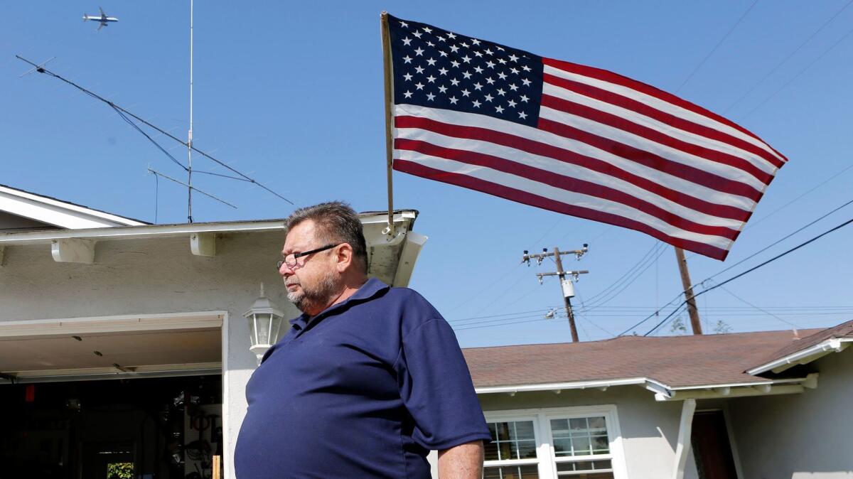 Mario Tabernig stands in his front yard in Huntington Beach as an airliner passes over on Thursday. Tabernig and other residents believe new Federal Aviation Administration air traffic procedures are causing excessive airplane noise in the city.