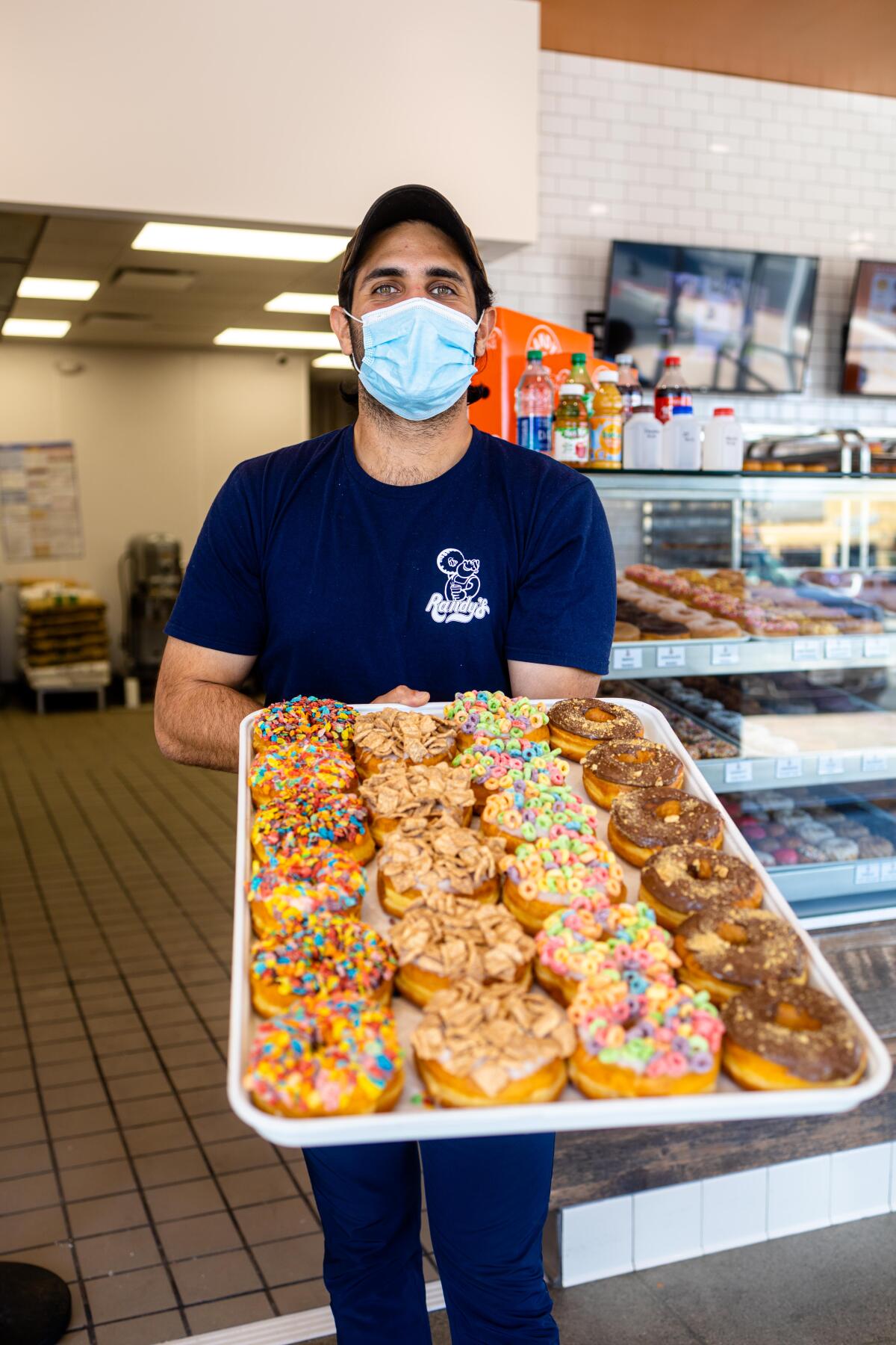 A photo of Kavon Azir holding a tray of colorful doughnuts inside his new location of Randy's Donuts.