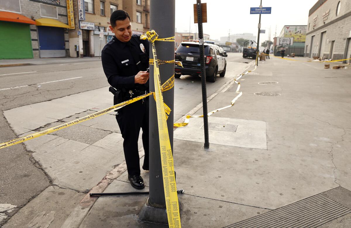 Los Angeles police officers take down tape where they have removed the belongings of a person they have detained on outstanding warrants on skid row last month.