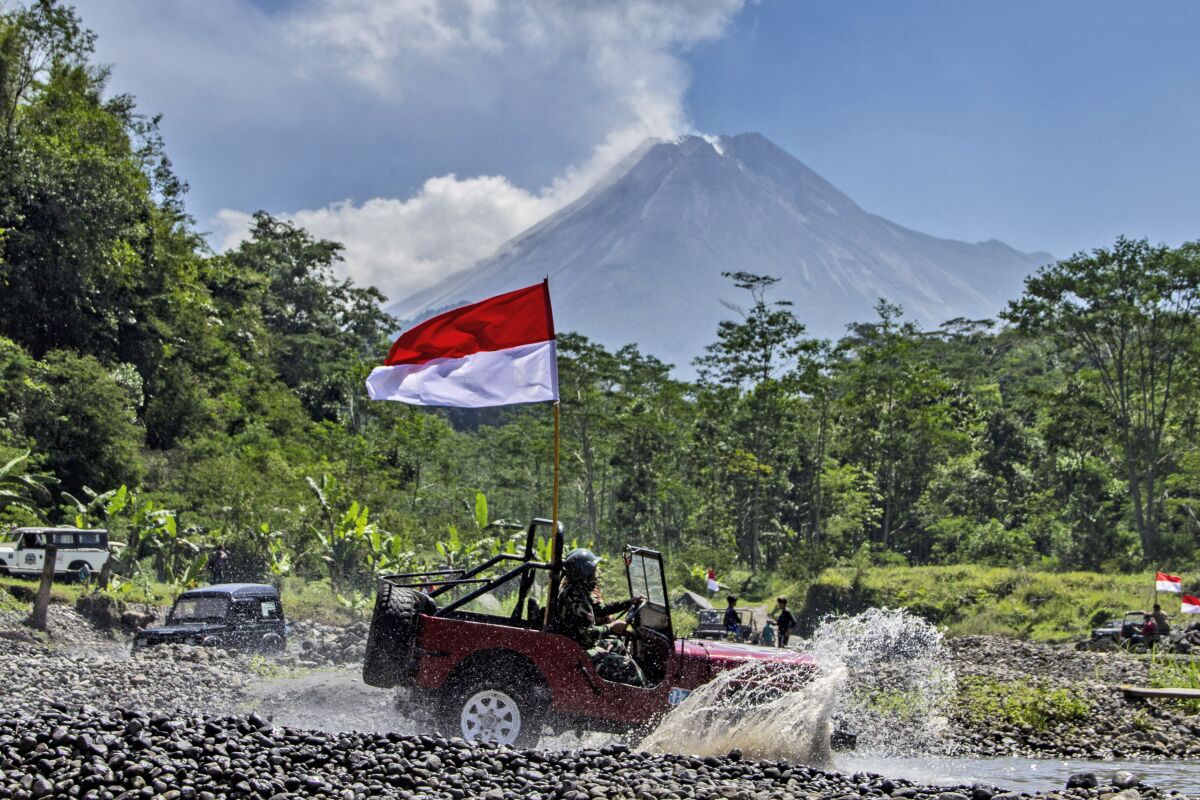 FILE - An Indonesian national Red-White flag waves from a car driven through an off-road track as Mount Merapi, one of the most active volcanoes in the country, is seen spewing volcanic smoke, during an Independence Day celebration in Sleman, Indonesia, Tuesday, Aug. 17, 2021. Dutch troops used “extreme violence” — often deliberately — during Indonesia's war for independence and military leaders and politicians in the Netherlands largely ignored the excesses, a long-running research project concluded in findings published Thursday, Feb. 17, 2022. In 2020, Dutch King Willem-Alexander formally apologized for his country’s aggression while on a state visit to Indonesia. (AP Photo/Slamet Riyadi, File)