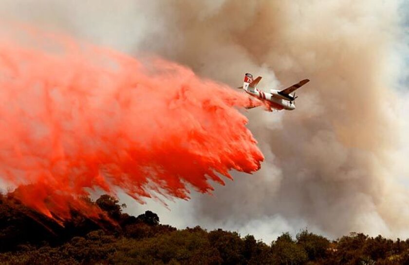 A plane drops Phos-Chek fire retardant to help slow the flames.