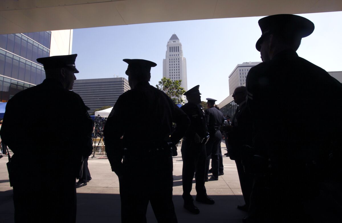 Silhouettes of several police officers are seen agains a background of downtown Los Angeles with the City Hall at the center.