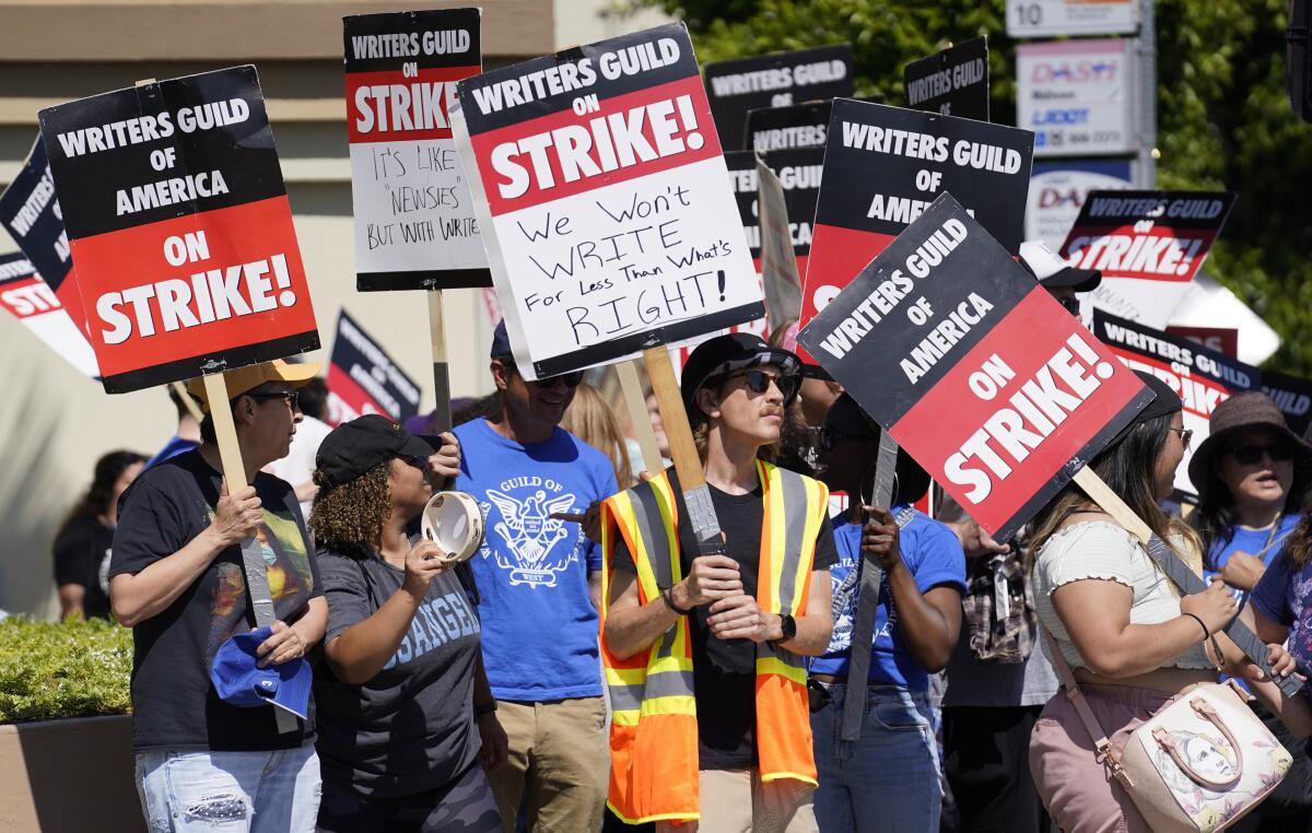 A group of people carrying picket signs that say, "Writers Guild of America on Strike"