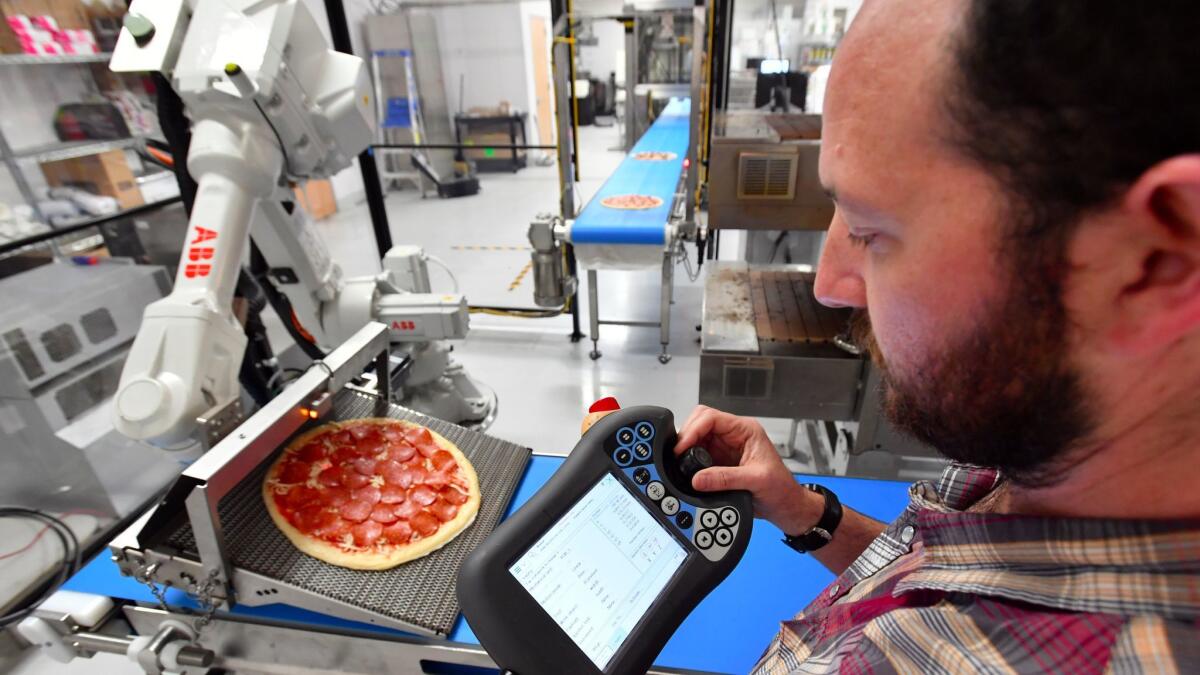 Josh Goldberg controls a robot whose sole purpose is to take a pizza off the conveyor belt and put it into an 800-degree oven.