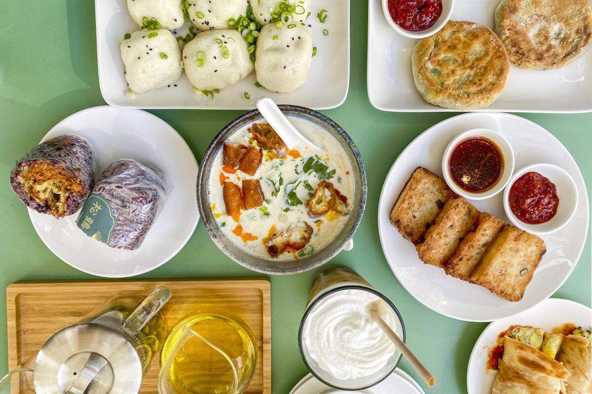 Overhead closeup of dishes on a table including a bowl of soup, sliced bread and dips on a plate, and a malt.