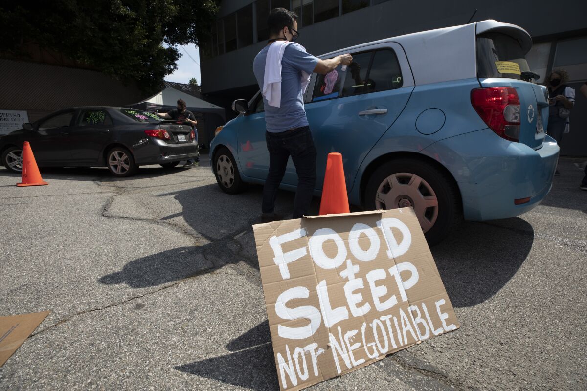 A man paints on a car window. Beside him, a sign reads, "Food & sleep not negotiable." 
