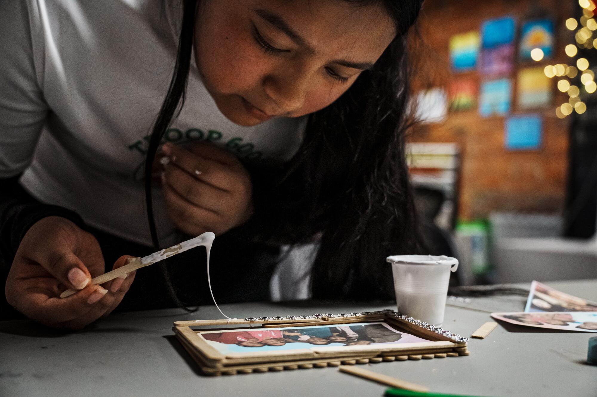 A girl spreads glue on a picture frame made of stick. 