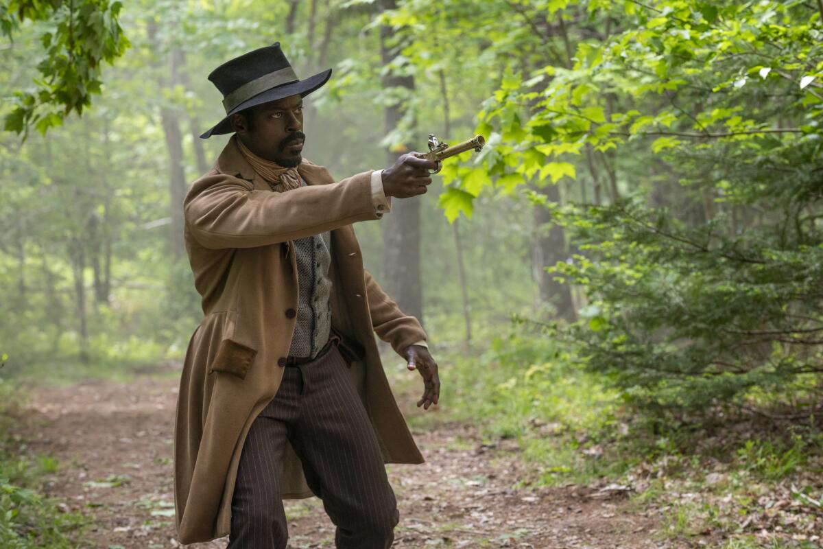 A man in a brown coat and black top hat holds out a gun.