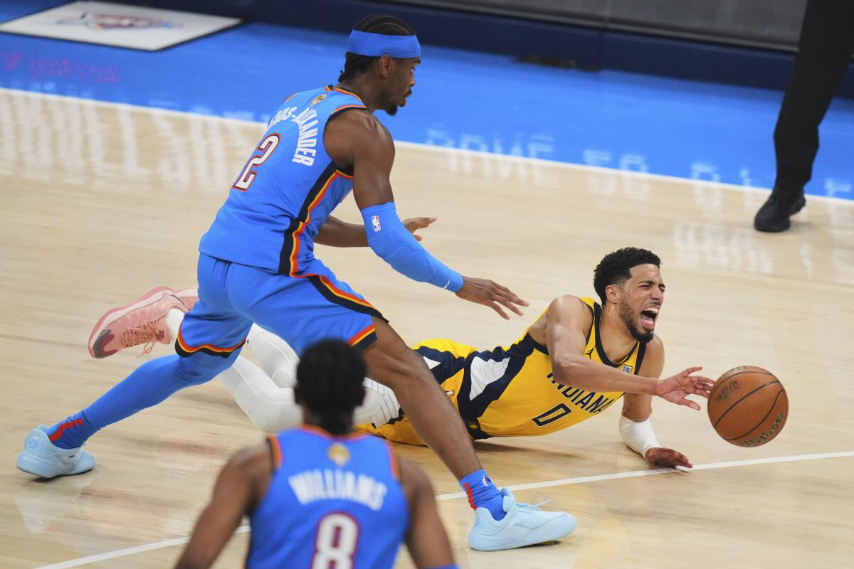 Tyrese Haliburton yells out and winces in pain as he lands horizontally on the court. Shai Gilgeous-Alexander leans over him