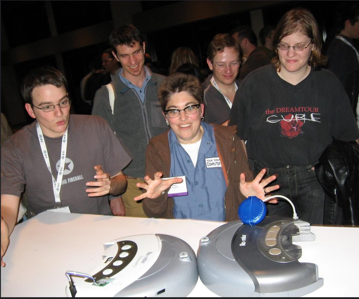 A group of people watches two robots on a table.