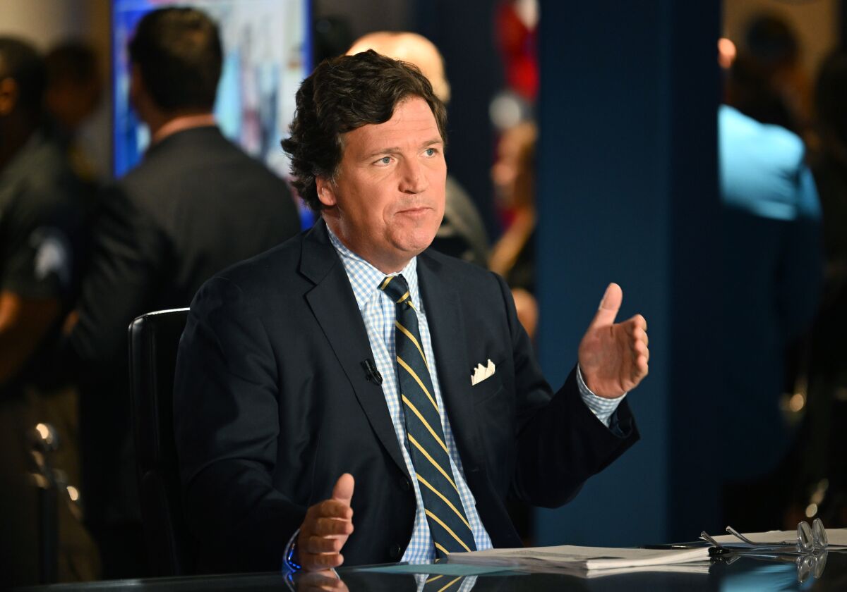 Tucker Carlson gestures while sitting at a desk.