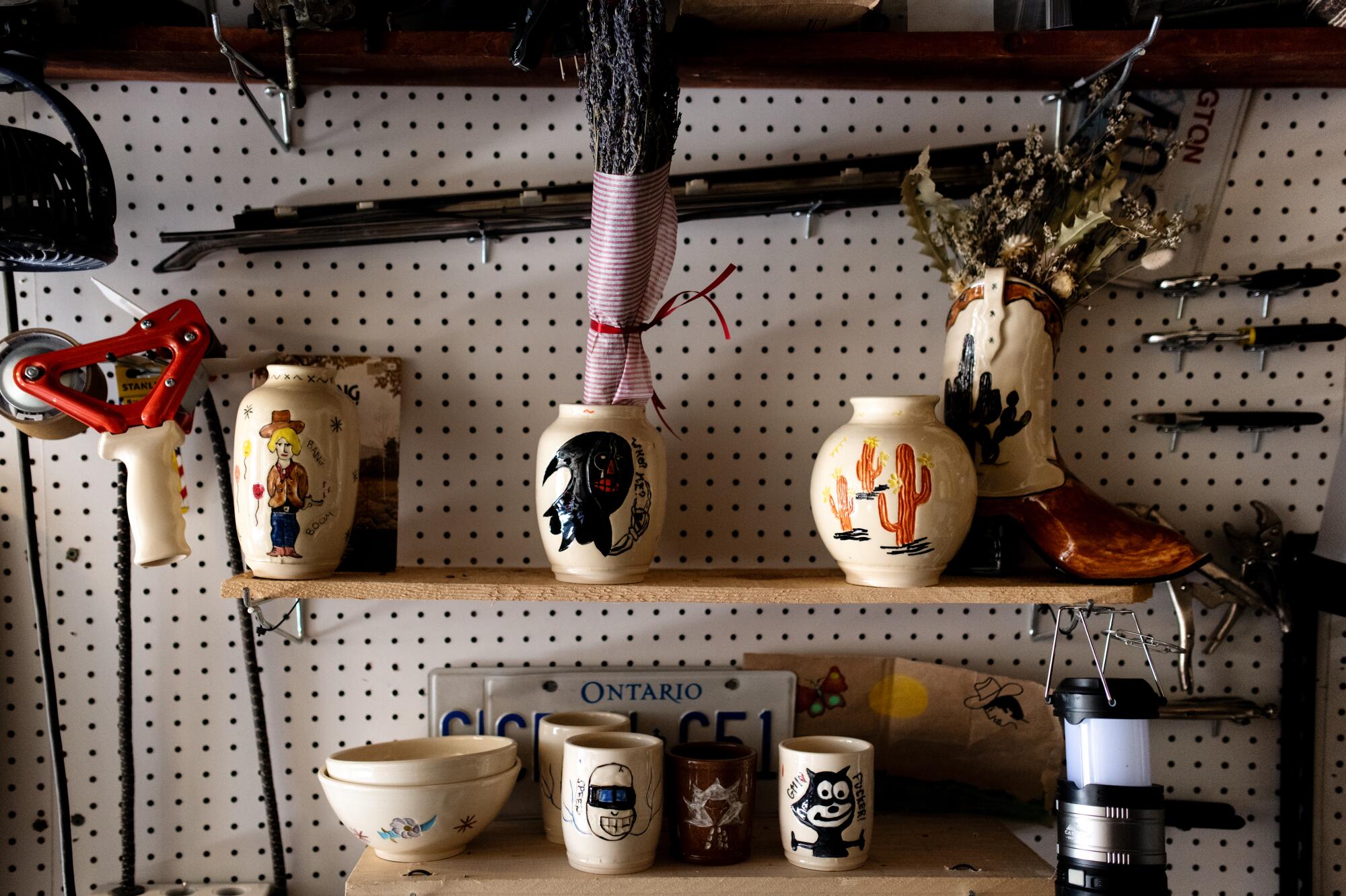 Ceramic vases, tumblers and bowls  on shelves in front of a pegboard wall