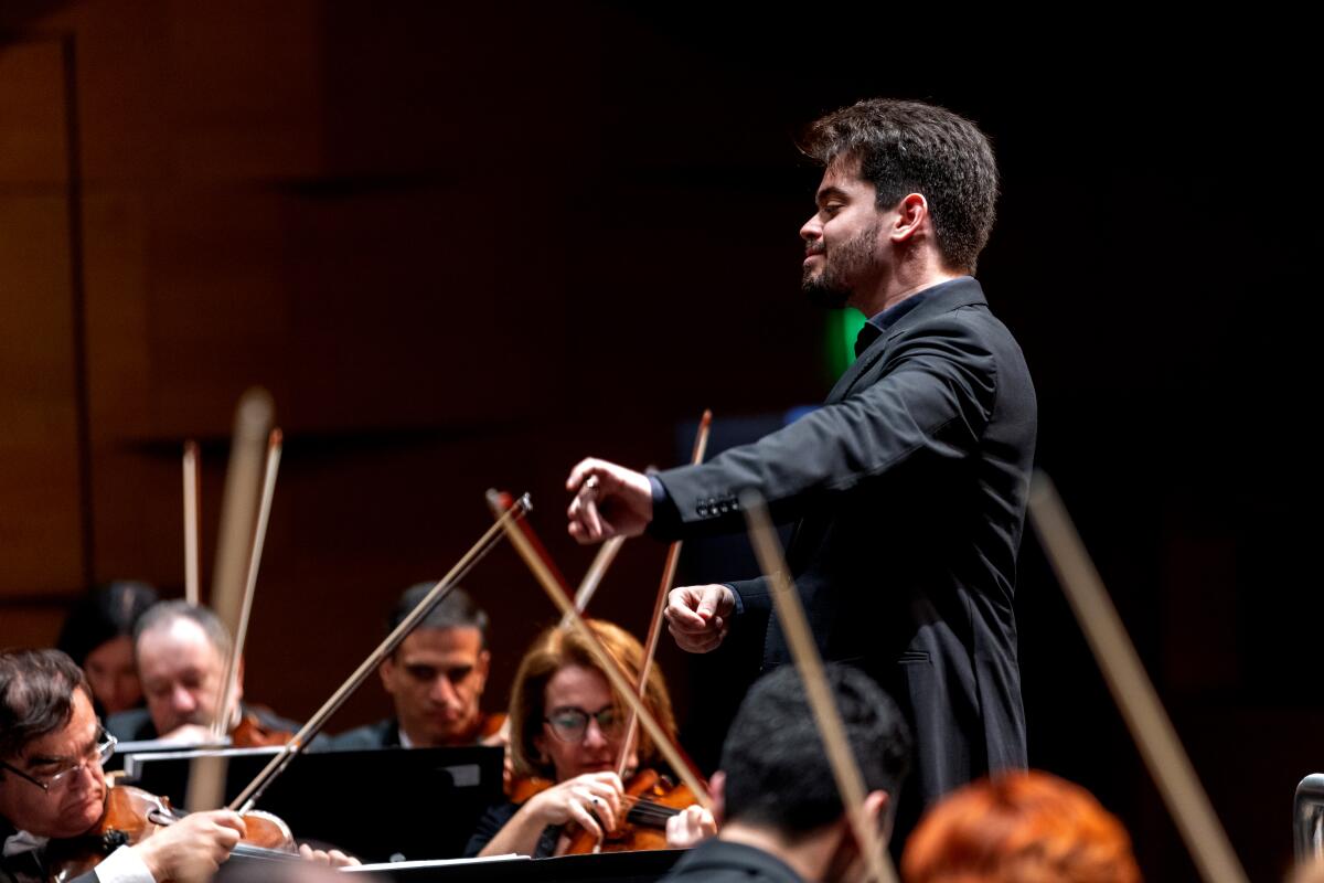 Lahav Shani is seen leading an orchestra from a conductor's podium