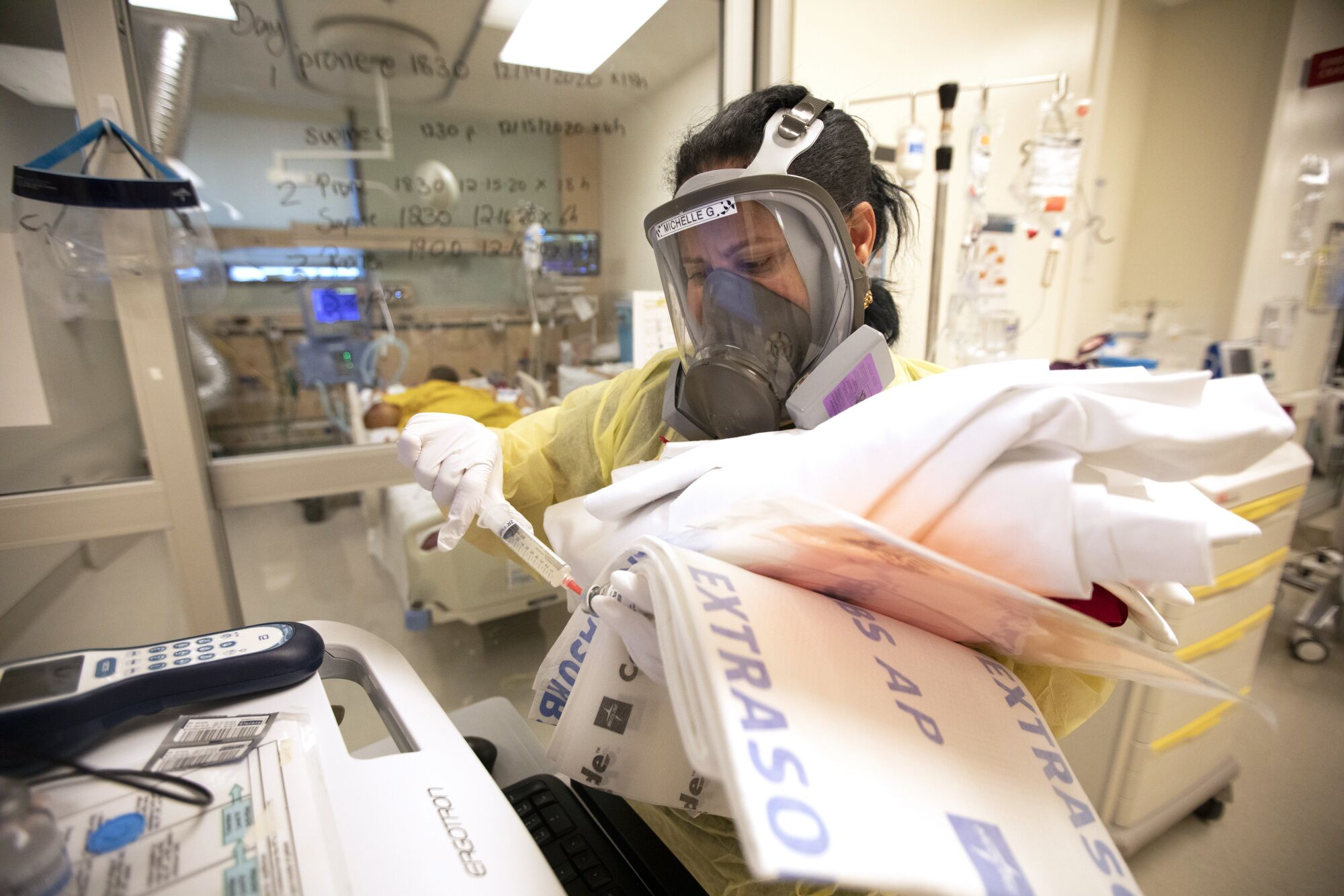 A nurse wearing a respirator mask stands with arms full of supplies.