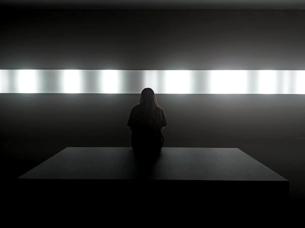 Light shining out of an LED panel on the wall, illuminating someone sitting in front of it in a dark room