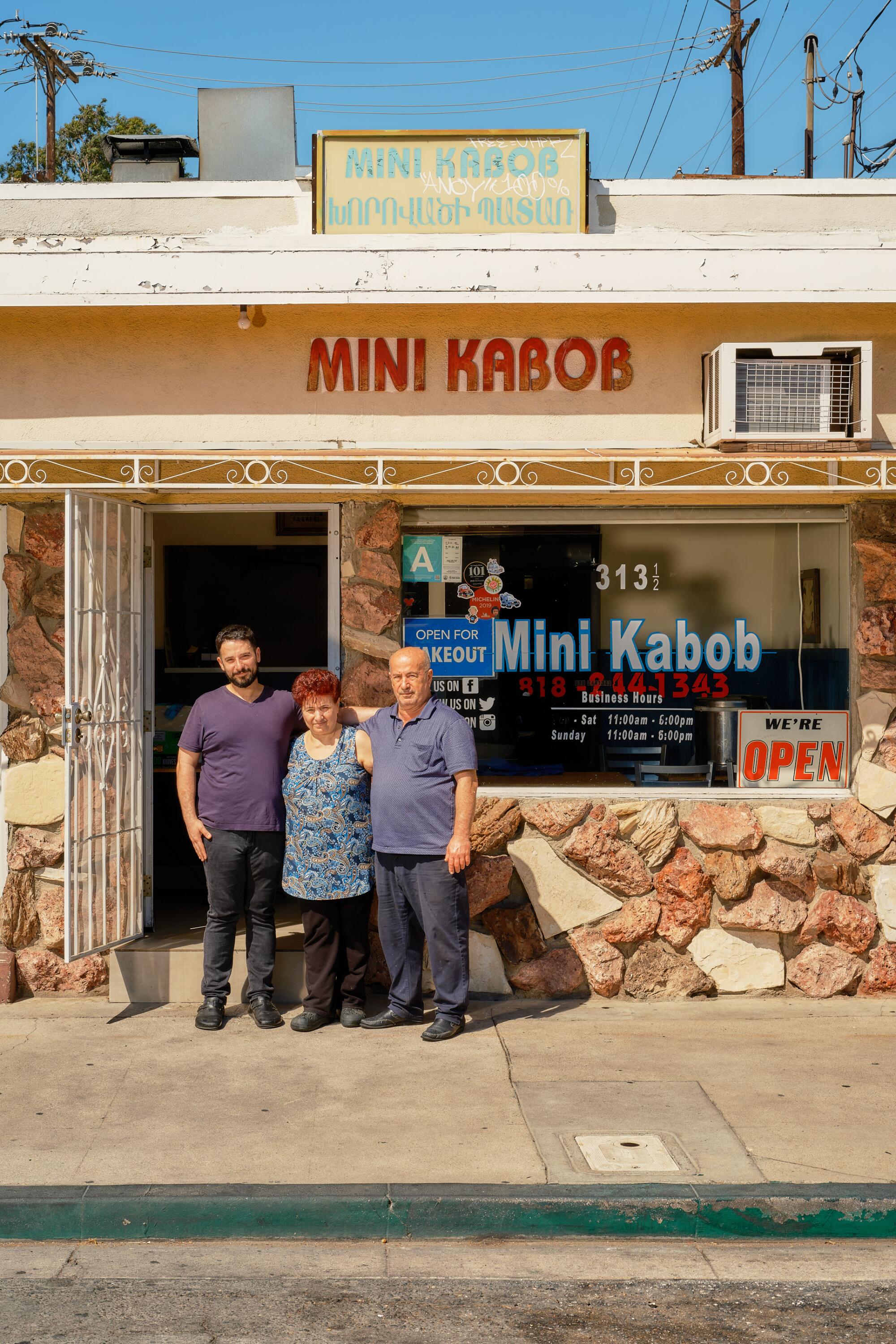 A family with their arms around each other stands in front of a small restaurant