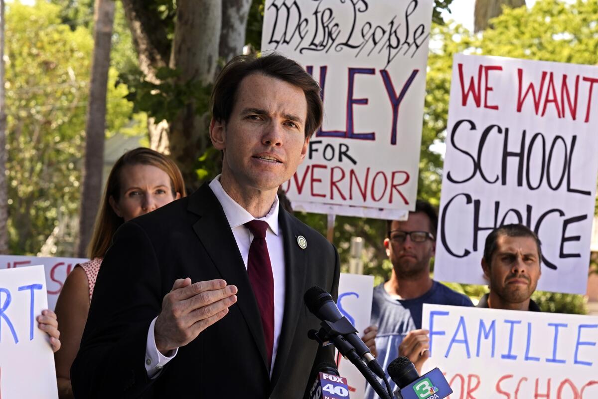 A man in a suit and tie stands in front of several people holding signs.