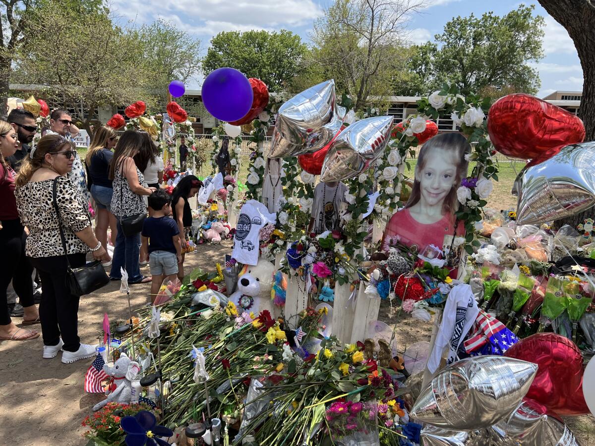 A large photo of a girl is surrounded by balloons and flowers at a makeshift memorial 