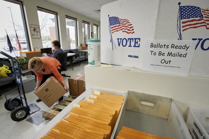 In this April 14, 2020 photo, Nadette Cheney picks up a box of printed ballots as others work on preparing mail-in ballots at the Lancaster County Election Committee offices in Lincoln, Neb. Officials in Nebraska are forging ahead with plans for the state’s May 12 primary despite calls from Democrats to only offer voting by mail and concerns from public health officials that in-person voting will help the coronavirus spread. (AP Photo/Nati Harnik)