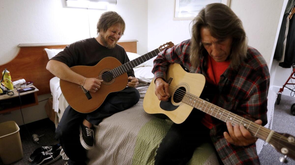 Michael Diehl, left, and Byron Pierce play their guitars after being placed in a motel room last month. They had been living in a homeless encampment along the Santa Ana River in Anaheim.
