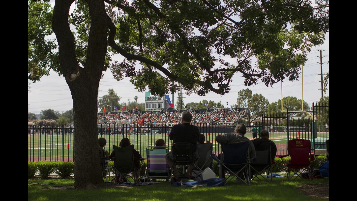 Fans watch a Division III matchup between Whitworth and La Verne at Ortmayer Stadium from the shade of a few trees.