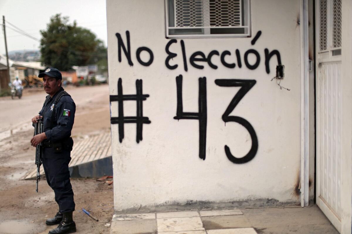 Un policía resguarda una de las calles en el estado de Guerrero, cerca de una pared con grafito donde se pide a la población no ir a votar y pregunta sobre los 43 normalistas desaparecidos en Ayotzinapa.