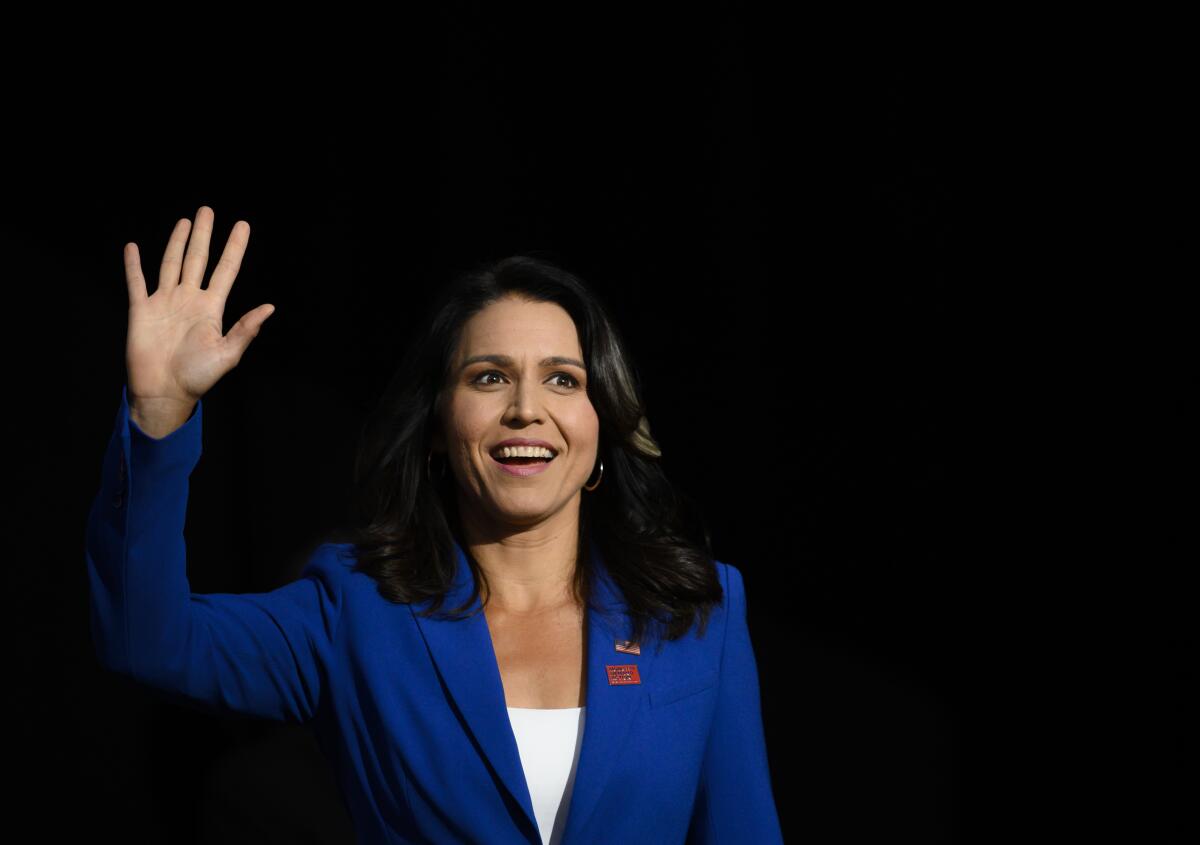 A woman wearing a blue blazer smiles and waves onstage