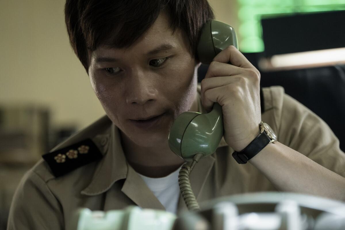A uniformed man holds a telephone receiver to his ear.