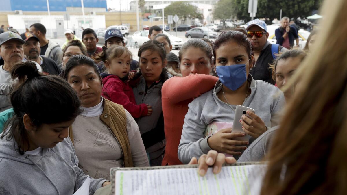 In this Oct. 23, 2018, photo, women in Tijuana look on as numbers and names are called to cross the border and request asylum in the United States.