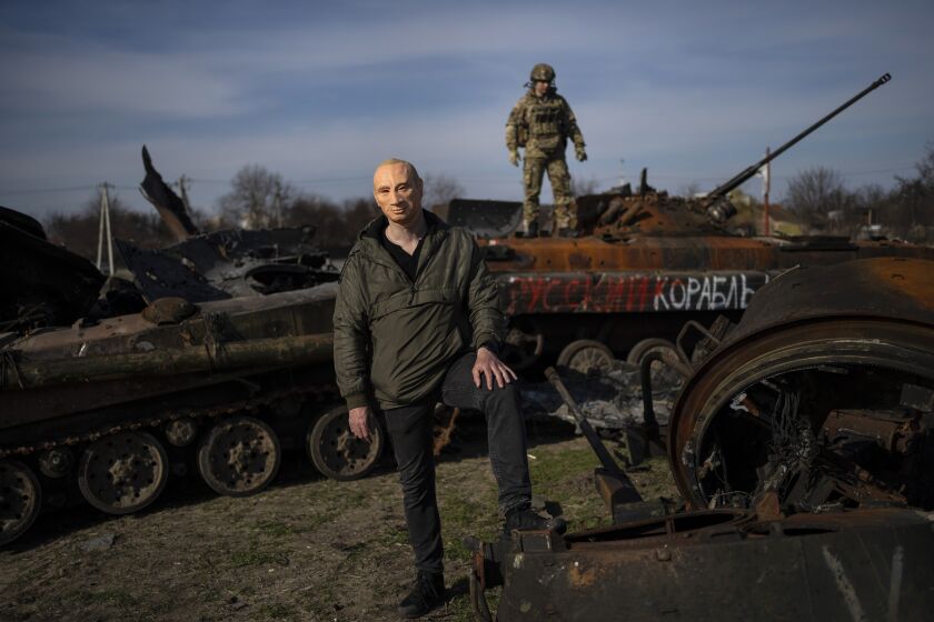 A civilian wears a Vladimir Putin mask as a spoof, while a Ukrainian soldier stands atop a destroyed Russian tank in Bucha, Ukraine, outside of Kyiv, on April 7, 2022. (AP Photo/Rodrigo Abd)
