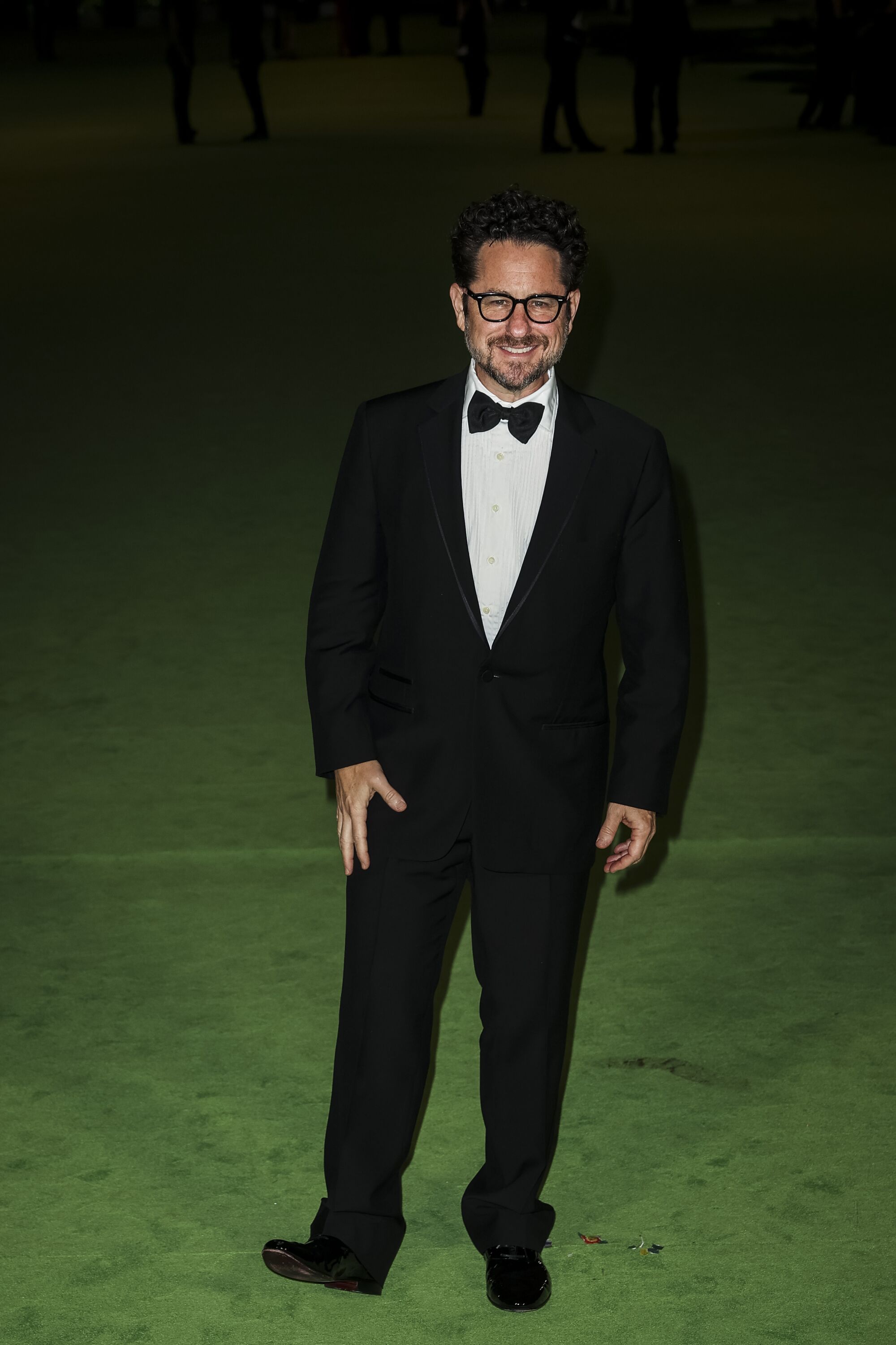 A man in a black tuxedo and bow tie posing on a green carpet